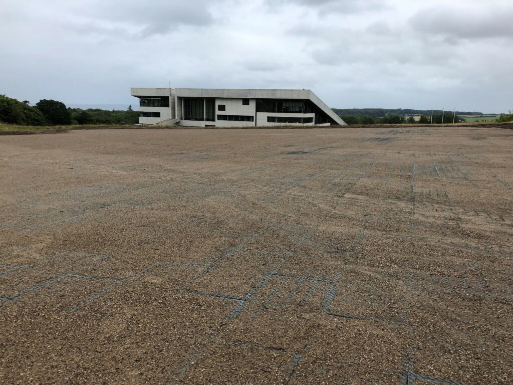 Moderne bygning ved stort grusområde under overskyet himmel